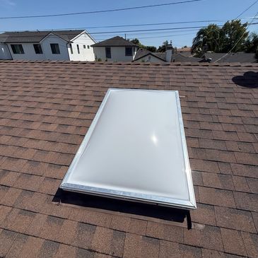 Skylight on a shingled roof under clear sky.