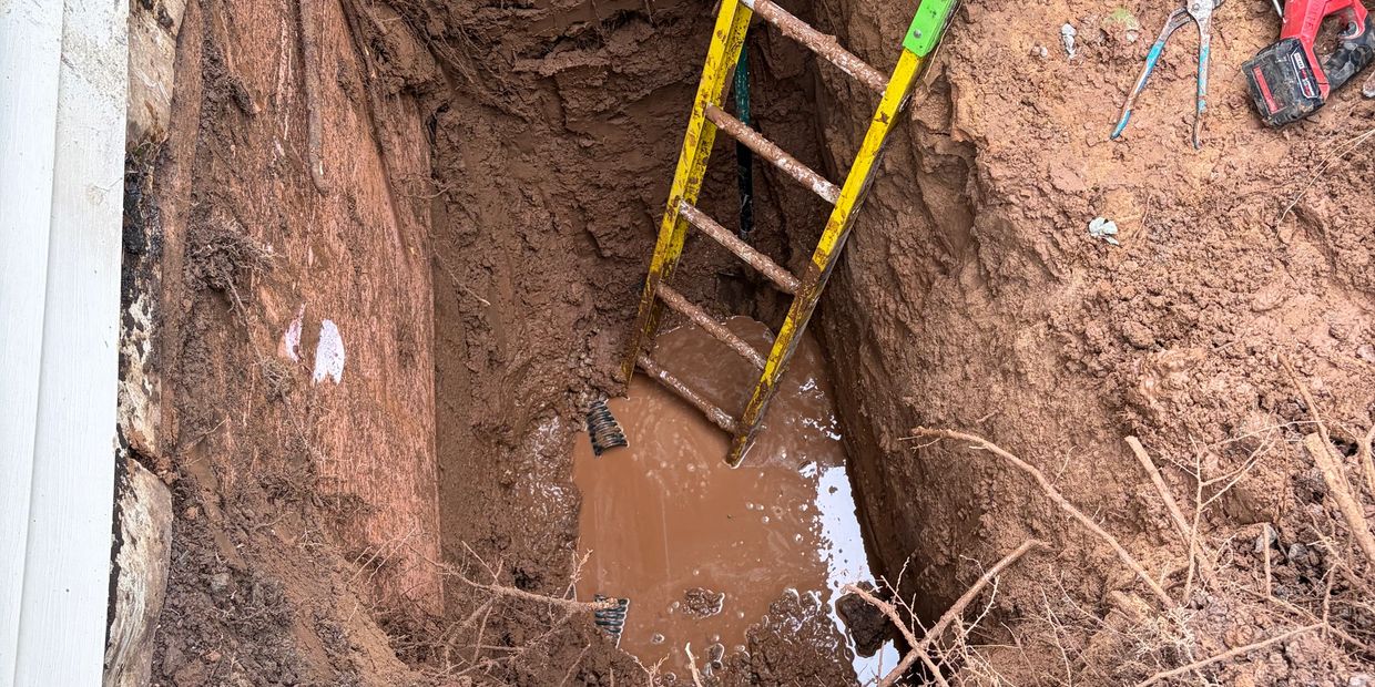 Mud-filled trench with a yellow ladder and tools nearby.