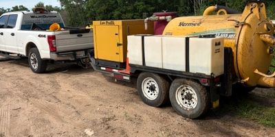 Pick-up truck towing construction equipment on dirt road.