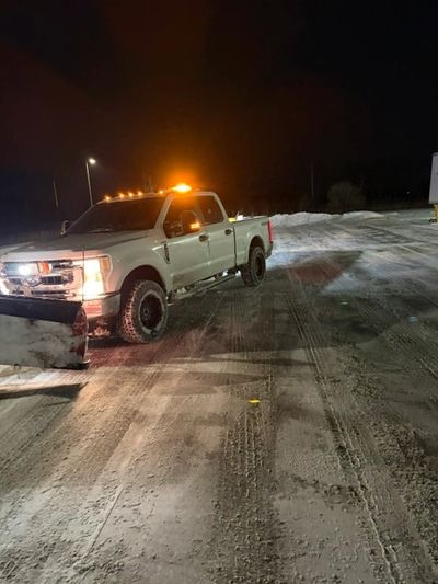 White truck with snow plow clearing snowy road at night.