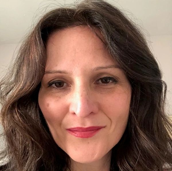 Woman with wavy brown hair and pink lipstick smiling gently.