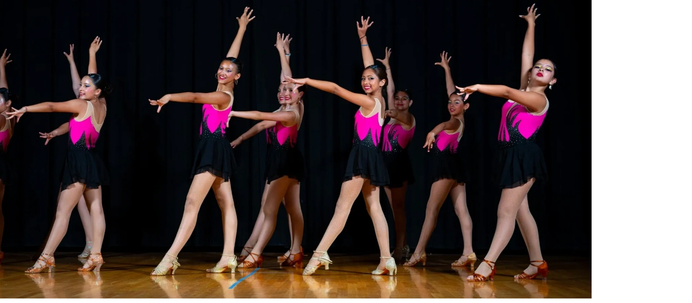 Young dancers in pink and black costumes performing in sync on stage.