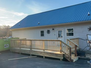 Man carrying a window frame near a house with a wooden ramp and large dumpster.