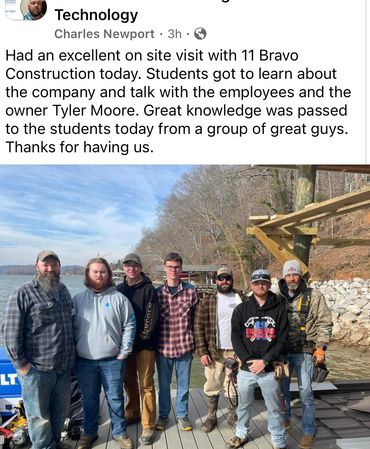 Construction team and students pose together outdoors by the water on a sunny day.