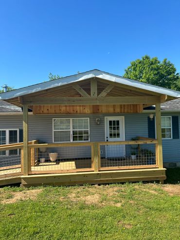 New wooden porch with railing attached to a blue house under clear sky.
