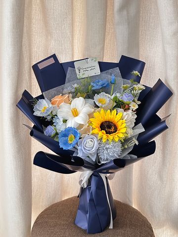 Elegant bouquet with sunflower, roses, and blue flowers wrapped in navy paper.