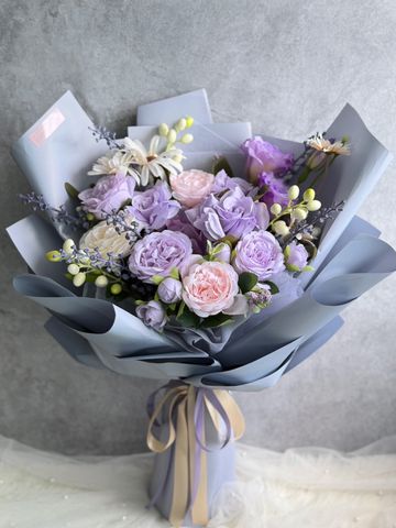Elegant bouquet of pastel purple and pink flowers wrapped in grey paper with a ribbon.