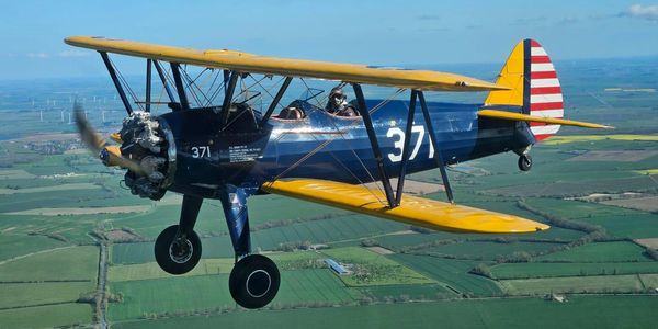 Yellow and blue vintage biplane flying over farmland.