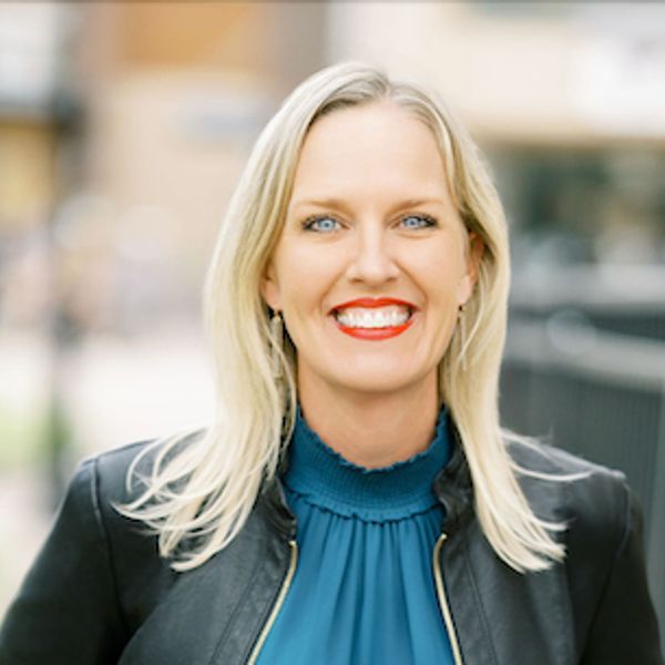 Smiling woman with blonde hair wearing a black leather jacket and blue top.