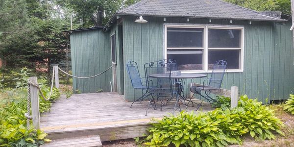 Wooden deck with metal chairs and a green cabin surrounded by trees.