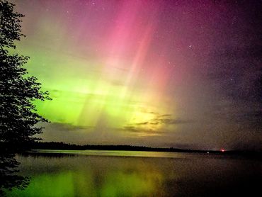 Vibrant northern lights glow green and pink over a calm lake at night.