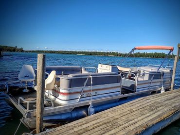 A pontoon boat docked at a wooden pier on a sunny day.