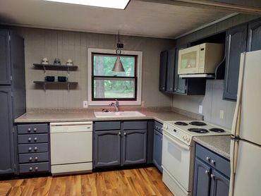 Cozy kitchen with gray cabinets, white appliances, and wood flooring under a skylight.