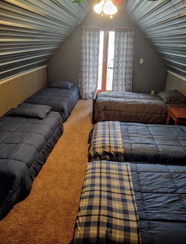 A cozy attic bedroom with four beds and patterned curtains.