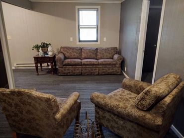 A cozy living room with patterned sofa and chairs, a side table, and a window.