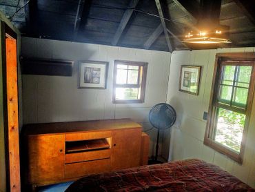 Cozy room with wooden furniture, two windows, and a standing fan.