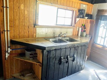 Rustic kitchen with a double sink, wooden cabinets, and natural light through a window and door.