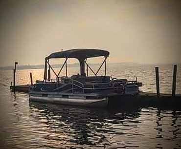 Pontoon boat docked on calm water during sunset.
