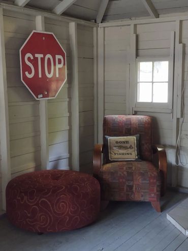 Cozy corner with a patterned armchair, ottoman, and a stop sign on a wooden wall.