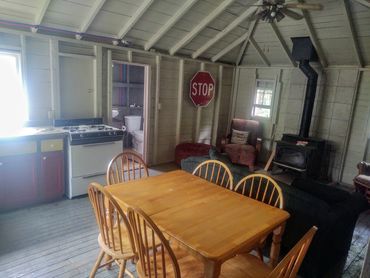 Rustic cabin interior with wooden dining table and six chairs, a stove, and a stop sign on the wall.