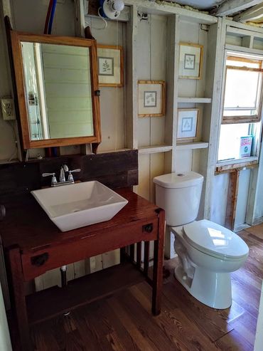 Rustic bathroom with wooden vanity and white toilet under unfinished walls.