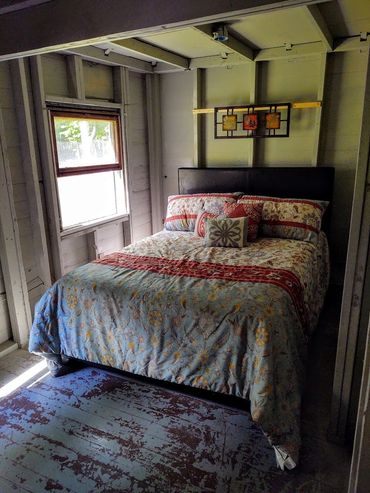 Cozy bed with floral bedding in a rustic, unfinished room with peeling blue floor paint.