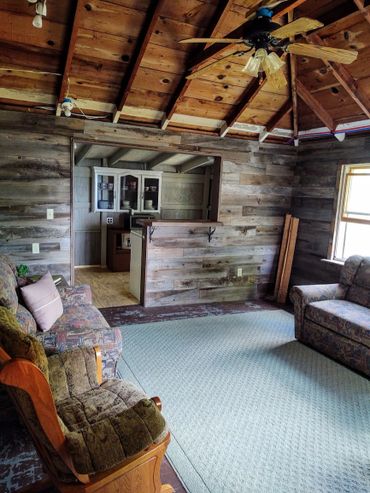 Rustic living room with wooden walls, ceiling fan, and cozy seating.