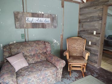 Cozy cabin corner with patterned loveseat, cushioned rocking chair, and rustic wall sign.