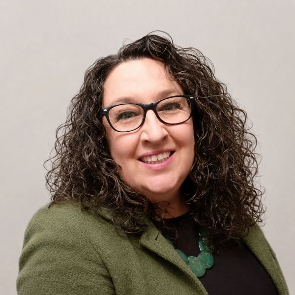 Smiling woman with curly hair and glasses.