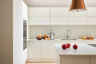 Minimalist white kitchen with fruits and modern appliances.