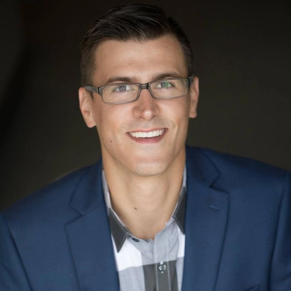 A smiling man wearing glasses and a blue blazer.