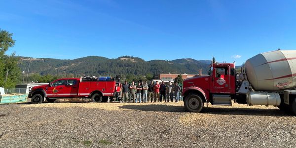Firefighters stand between two red emergency vehicles under a clear blue sky.