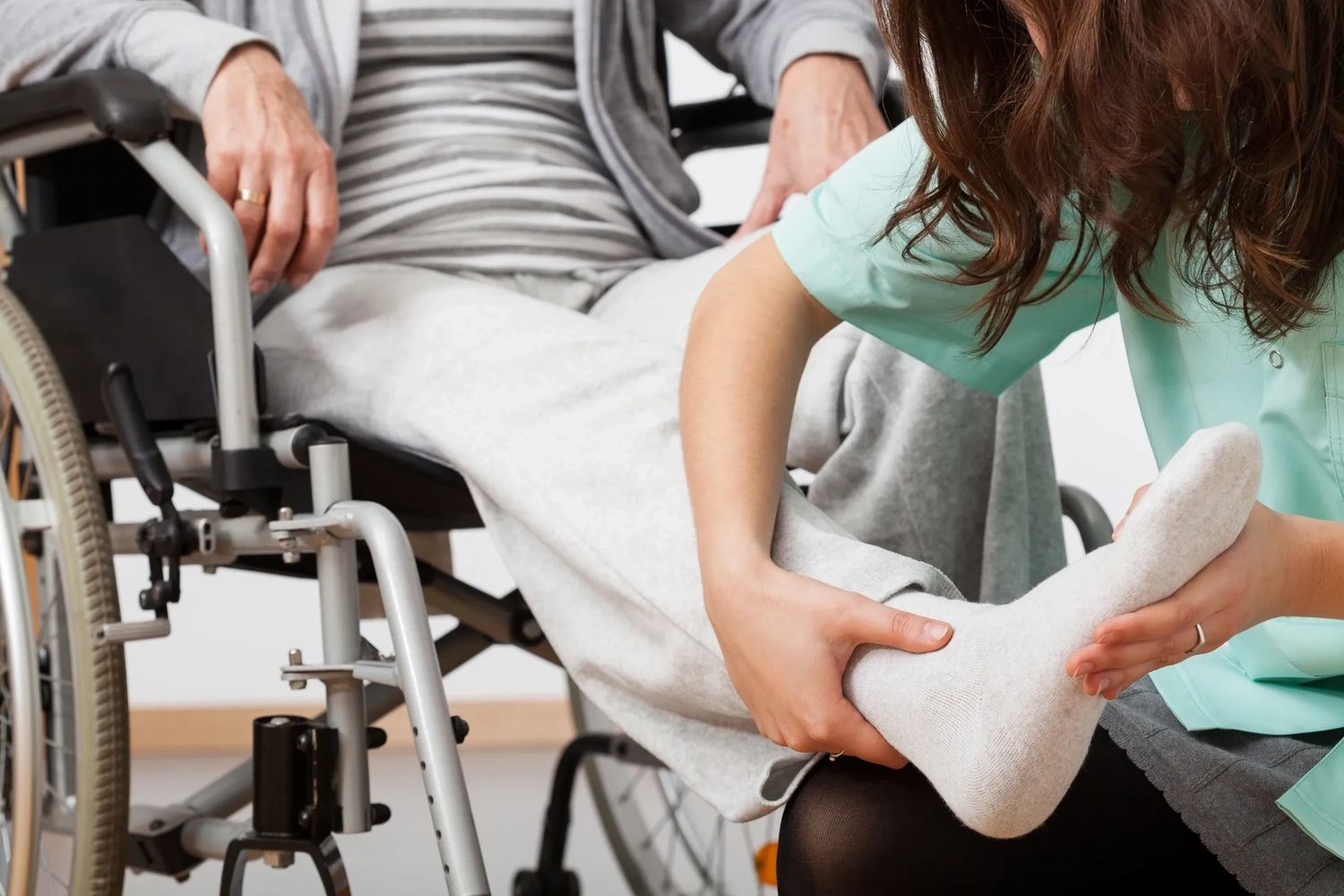 Caregiver assisting a person in a wheelchair by holding their foot gently.