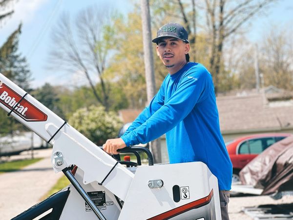 Man in a blue shirt operating a Bobcat machine outdoors.
