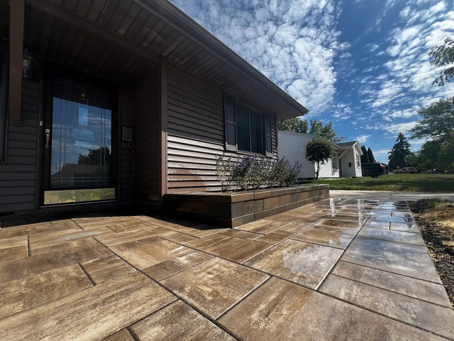 Wet tiled patio leading to a brown house under a partly cloudy sky.