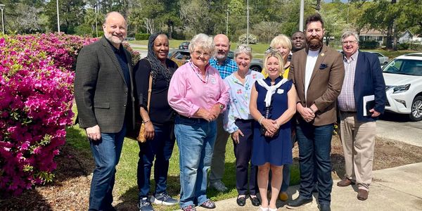 Group photo of ten diverse people outdoors on a sunny day.