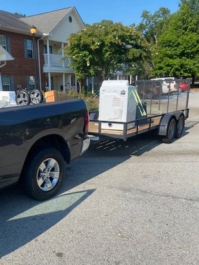 A black pickup truck towing a trailer with appliances in a residential area.