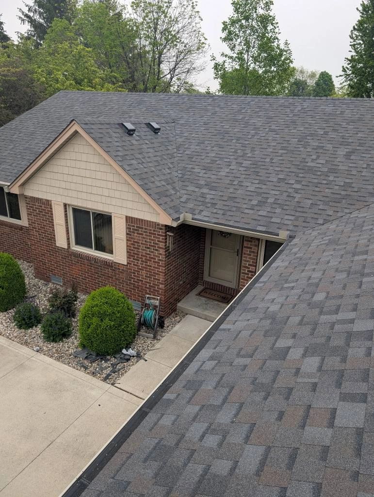 View of a brick house with a gray shingle roof and landscaped front yard.