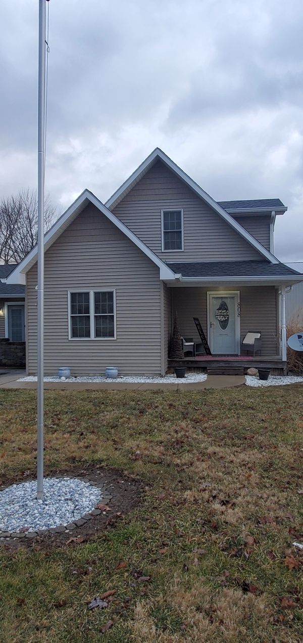 Cozy beige house with a small front porch and a flagpole in the yard under a cloudy sky.