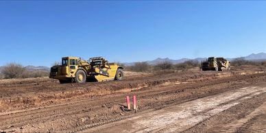 Two yellow construction vehicles leveling dirt on a clear day.
