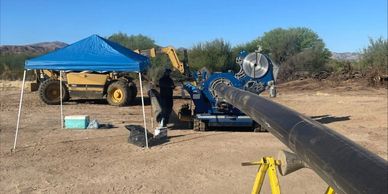 Construction site with machinery and a long pipe under a blue canopy.