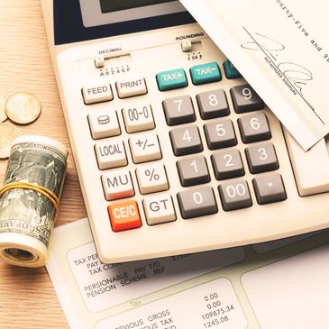 Calculator with cash, coins, a paycheck, and financial documents on a wooden surface.