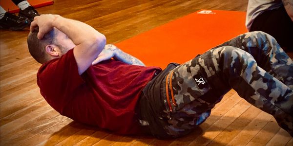 Man doing sit-ups on a wooden floor wearing a red shirt and camo pants.