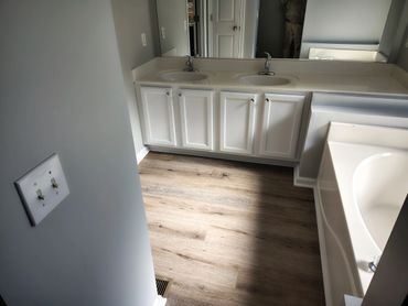 Modern bathroom with double sinks, white cabinetry, and wood-look flooring.