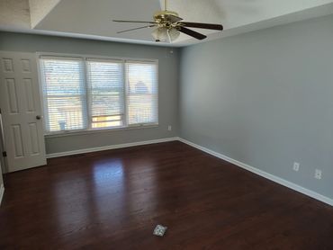 Empty room with wooden floor and ceiling fan under daylight.