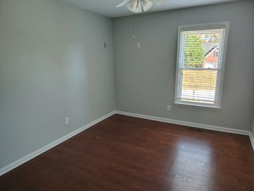 Empty room with gray walls, wooden floor, and a window with blinds.