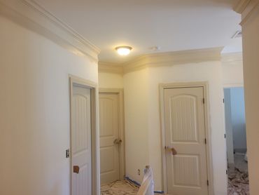 Interior hallway with three beige doors and crown molding undergoing painting.