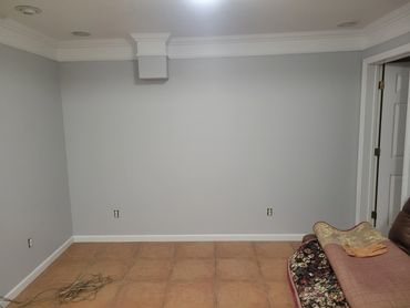 Empty room with tiled floor and gray walls, partially covered carpet and gloves on a chair.