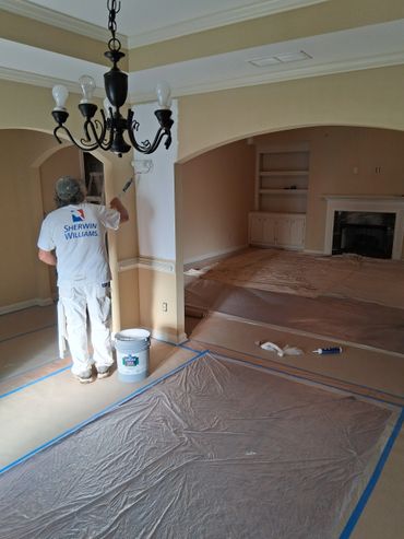 Painter in Sherwin Williams shirt painting a wall white indoors.