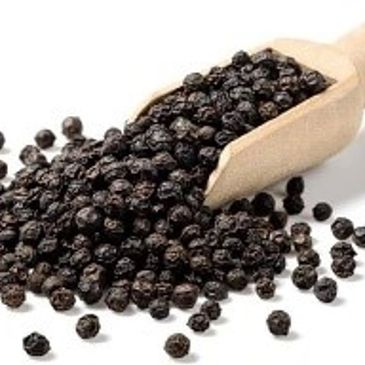 Close-up of black peppercorns spilling from a wooden scoop.